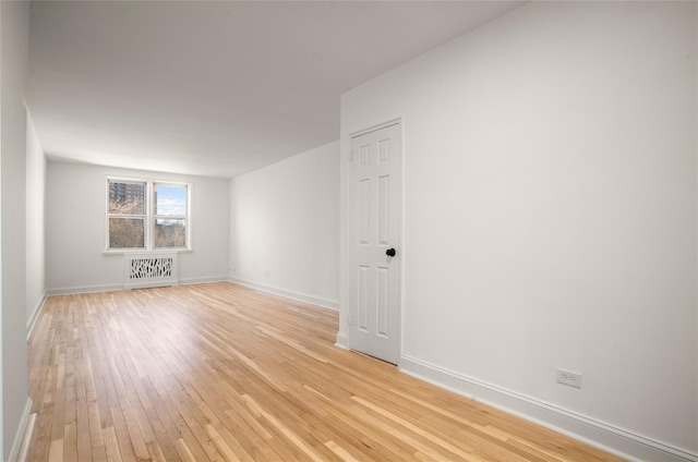 empty room with baseboards, light wood finished floors, and radiator