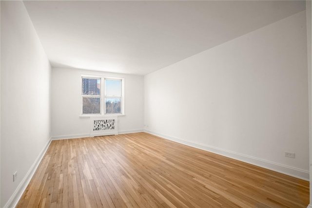 spare room featuring baseboards, light wood-style flooring, and radiator