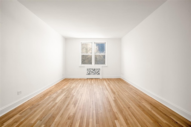 spare room with light wood-type flooring, radiator heating unit, and baseboards