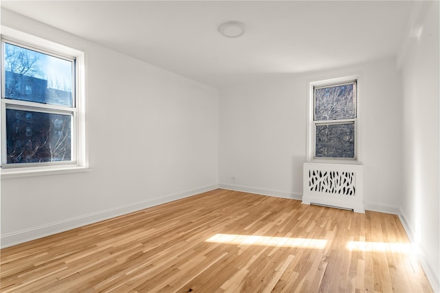 unfurnished room featuring radiator, light wood finished floors, and baseboards