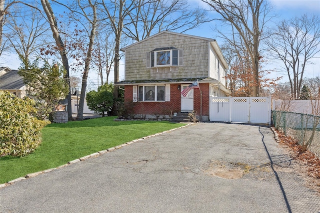 colonial inspired home with a front lawn, driveway, a gate, fence, and brick siding