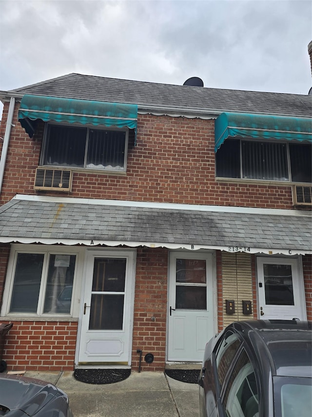 multi unit property featuring a shingled roof and brick siding