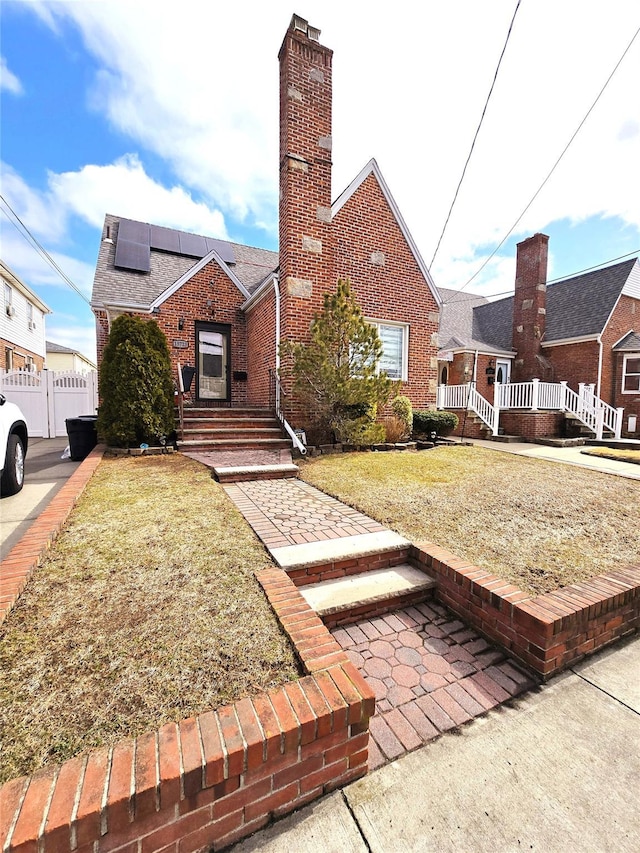 view of front of home featuring roof mounted solar panels, a chimney, a front lawn, and brick siding