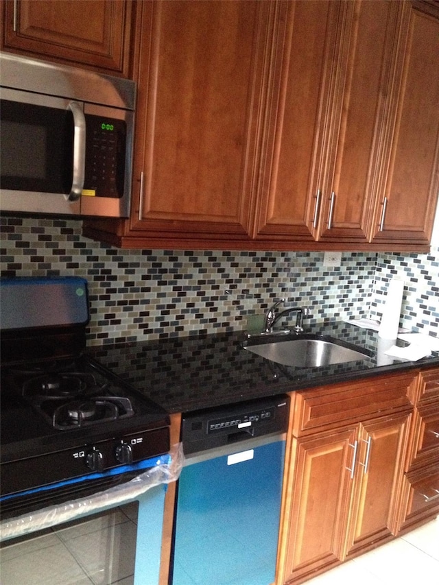 kitchen with appliances with stainless steel finishes, brown cabinets, dark stone countertops, a sink, and backsplash