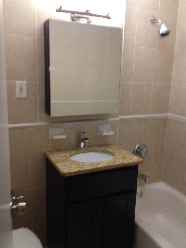 full bath with washtub / shower combination, toilet, vanity, and tile walls