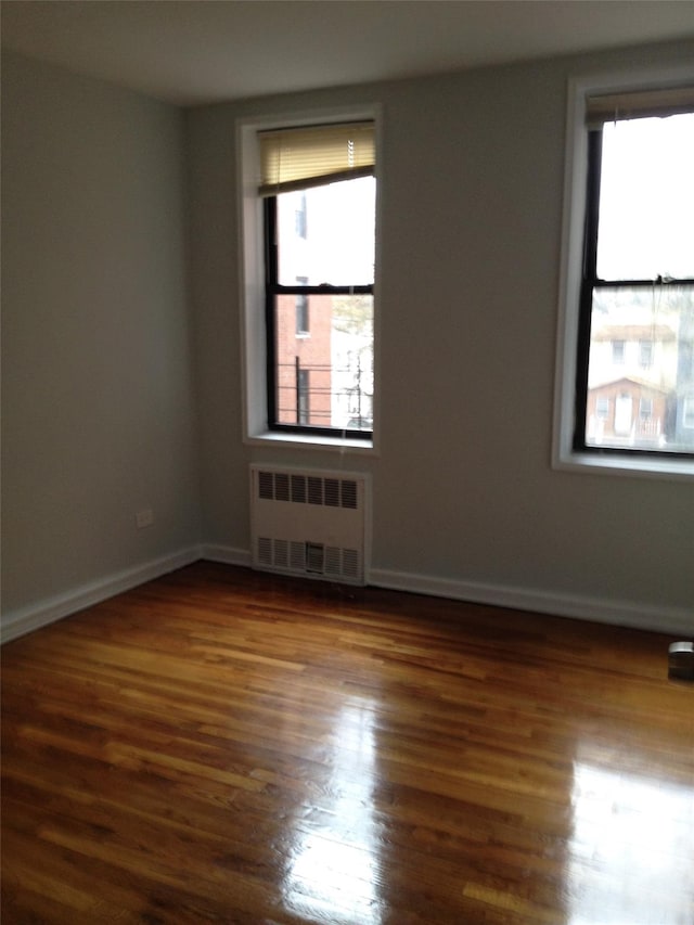 unfurnished room featuring a healthy amount of sunlight, dark wood-style floors, radiator heating unit, and baseboards