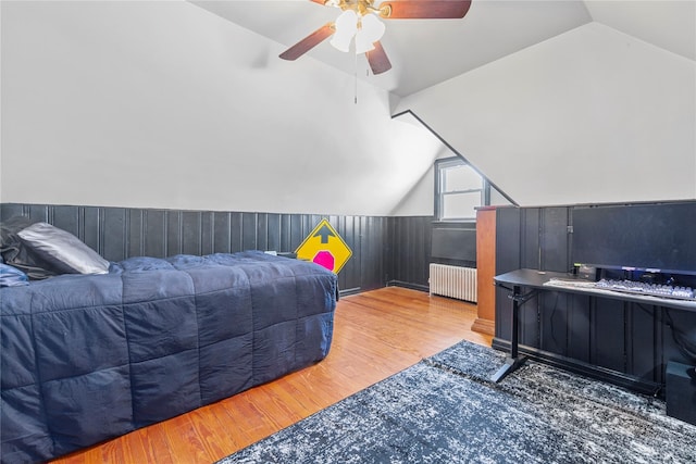 bedroom featuring wooden walls, a ceiling fan, radiator, wood finished floors, and vaulted ceiling