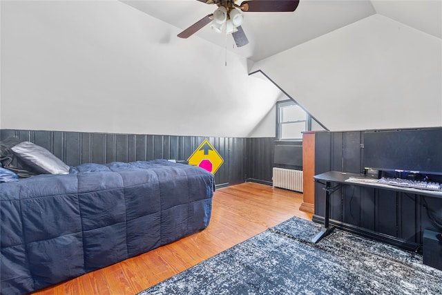 bedroom featuring lofted ceiling, wood walls, wood finished floors, a ceiling fan, and radiator heating unit