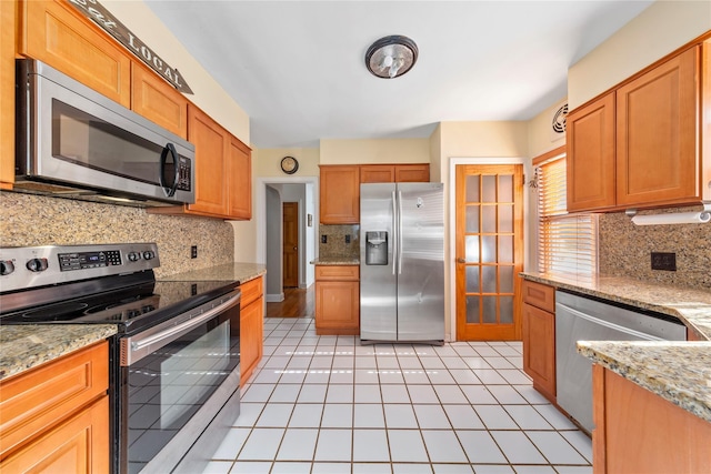 kitchen with light tile patterned floors, appliances with stainless steel finishes, light stone counters, and backsplash