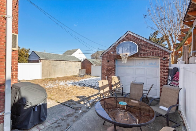 view of patio featuring a detached garage, grilling area, outdoor dining space, fence, and an outdoor structure