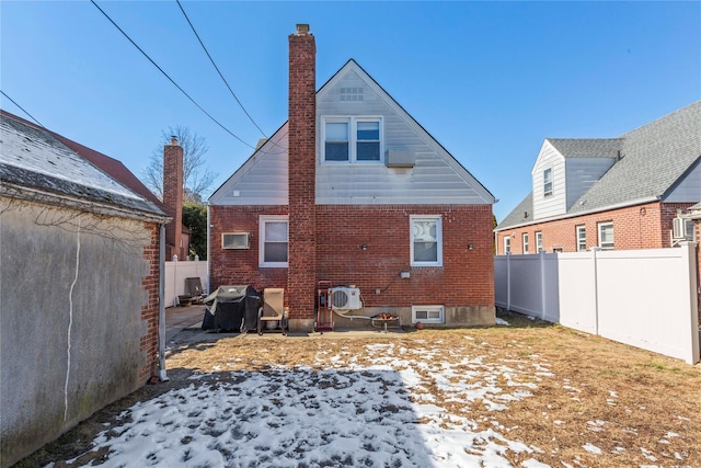 rear view of house with ac unit, a chimney, brick siding, and a fenced backyard