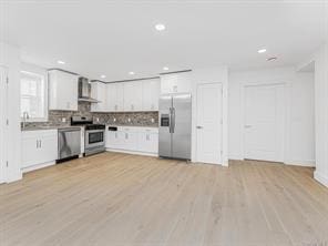 kitchen featuring stainless steel appliances, white cabinets, light wood-style flooring, and tasteful backsplash