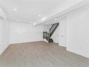 below grade area featuring wood finished floors, a wall mounted AC, baseboards, and stairs