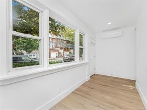 spare room with light wood-type flooring, baseboards, and a wall mounted air conditioner