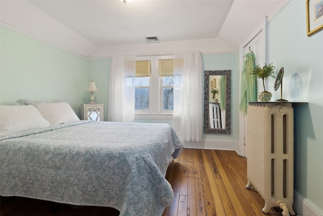 bedroom featuring hardwood / wood-style floors, vaulted ceiling, radiator heating unit, and visible vents