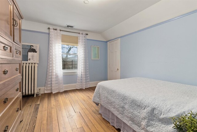 bedroom with baseboards, visible vents, lofted ceiling, light wood-style flooring, and radiator heating unit