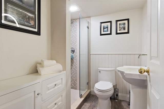 bathroom with toilet, wainscoting, a stall shower, wood finished floors, and a sink