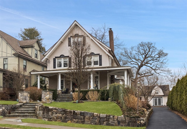 view of front of home featuring a chimney, a porch, and a front yard