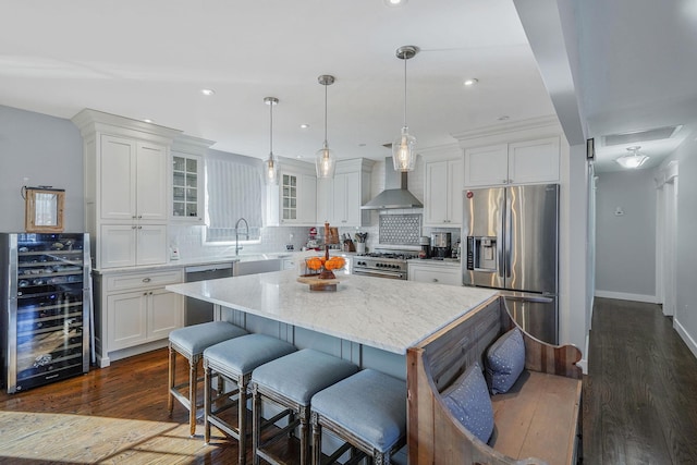 kitchen with stainless steel appliances, wine cooler, white cabinets, and wall chimney range hood