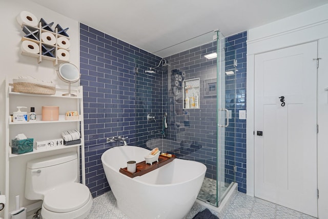 bathroom with a freestanding bath, tile walls, a shower stall, and toilet