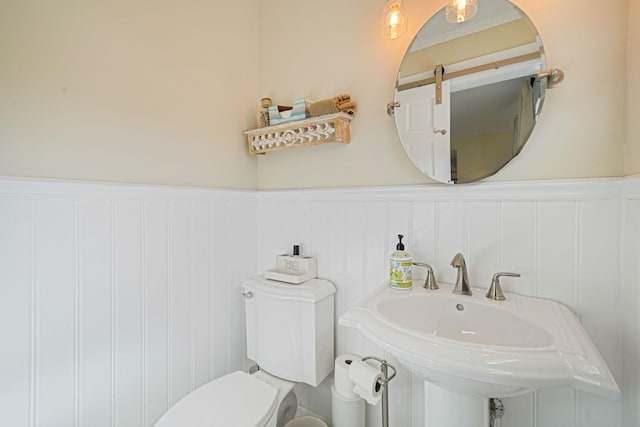 bathroom with a wainscoted wall, toilet, and a sink