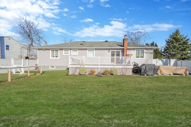 rear view of house with a chimney, a lawn, a wooden deck, and a fenced backyard