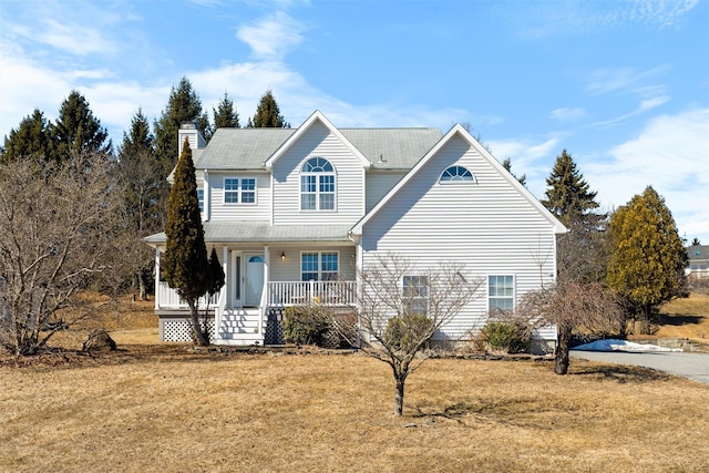 traditional-style house featuring covered porch, a chimney, and a front lawn