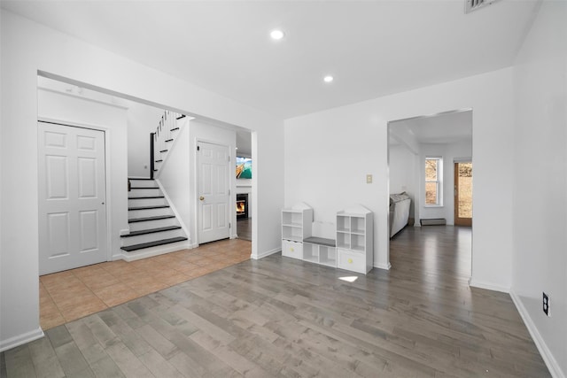 foyer featuring a lit fireplace, stairs, wood finished floors, and recessed lighting