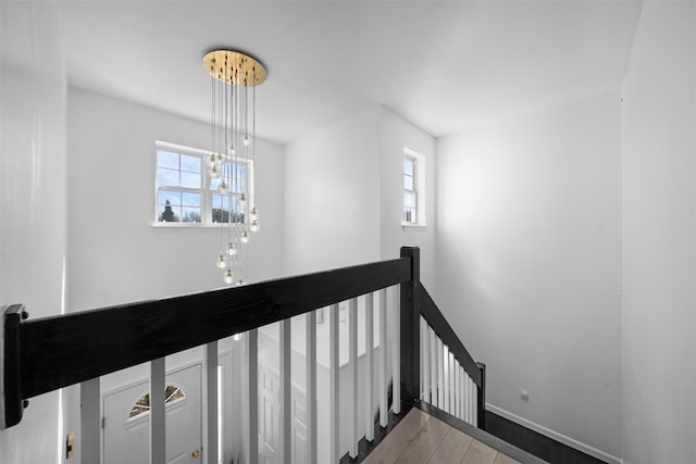 stairs with an inviting chandelier, plenty of natural light, baseboards, and wood finished floors