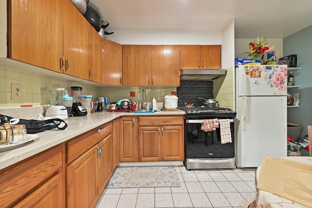 kitchen with light countertops, range hood, stainless steel range with gas cooktop, freestanding refrigerator, and brown cabinets