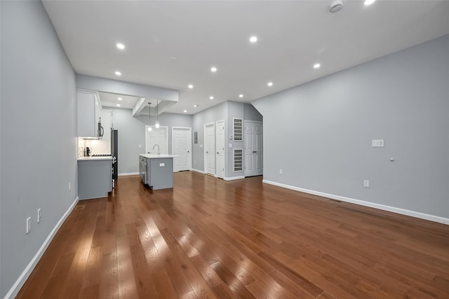 unfurnished living room featuring dark wood-style floors, baseboards, a sink, and recessed lighting