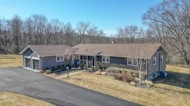 ranch-style home with a shingled roof, a front yard, central AC unit, a garage, and stone siding