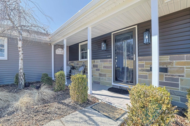 view of exterior entry with stone siding and a porch