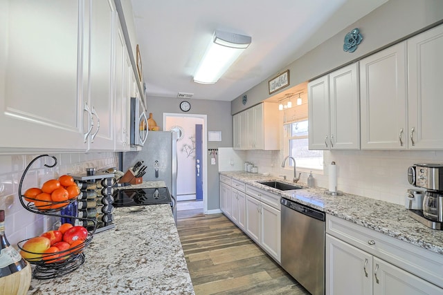 kitchen with a sink, decorative backsplash, stainless steel appliances, white cabinets, and light wood-type flooring