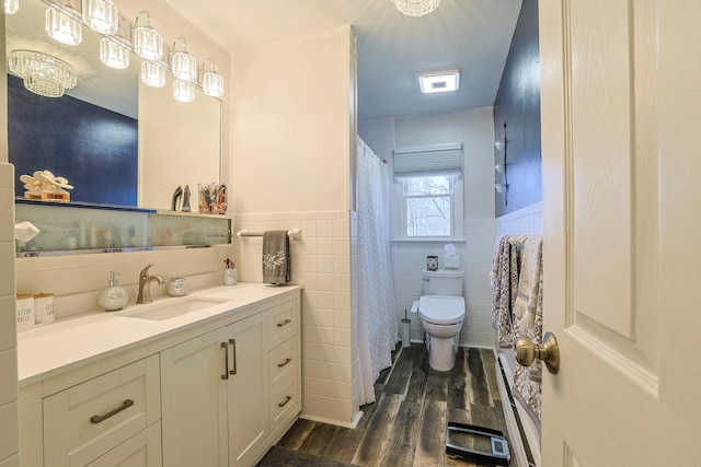 bathroom with toilet, wood finished floors, tile walls, wainscoting, and vanity