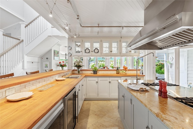 kitchen featuring extractor fan, beverage cooler, butcher block countertops, white cabinets, and rail lighting