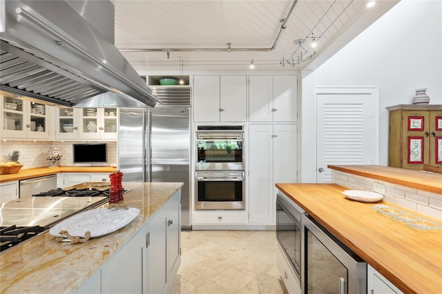 kitchen featuring wine cooler, built in appliances, island exhaust hood, wooden counters, and backsplash