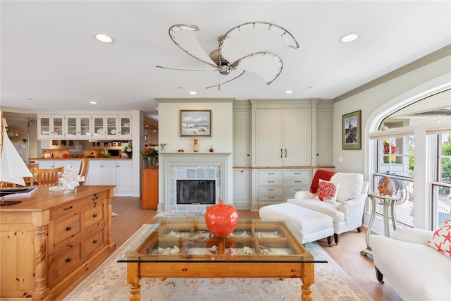 living room featuring recessed lighting, a tiled fireplace, light wood-style flooring, and crown molding