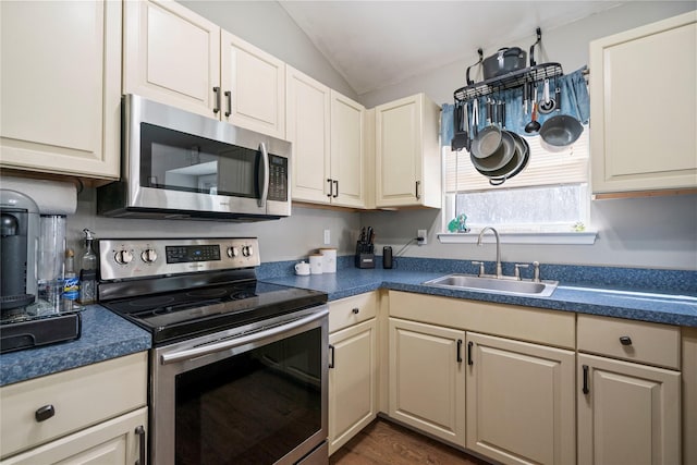 kitchen featuring dark countertops, a sink, vaulted ceiling, stainless steel appliances, and dark wood-style flooring