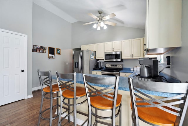 kitchen featuring dark countertops, ceiling fan, a kitchen breakfast bar, dark wood-style floors, and stainless steel appliances