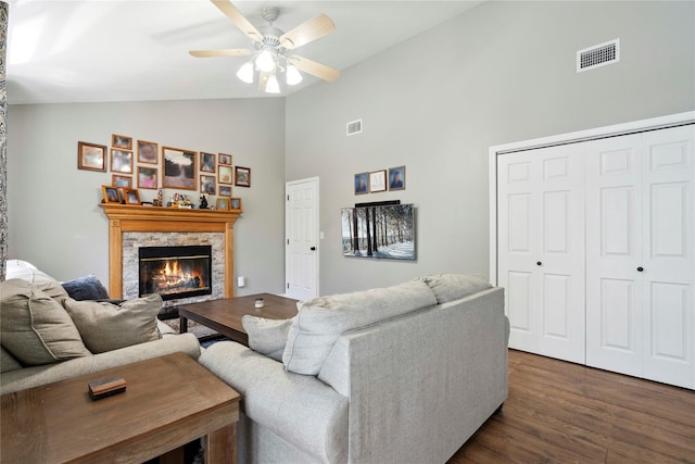 living room featuring dark wood-style floors, visible vents, a stone fireplace, and ceiling fan