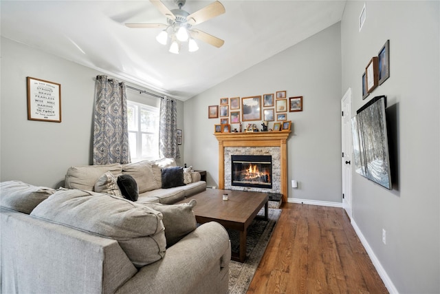 living room with visible vents, baseboards, lofted ceiling, a stone fireplace, and wood finished floors