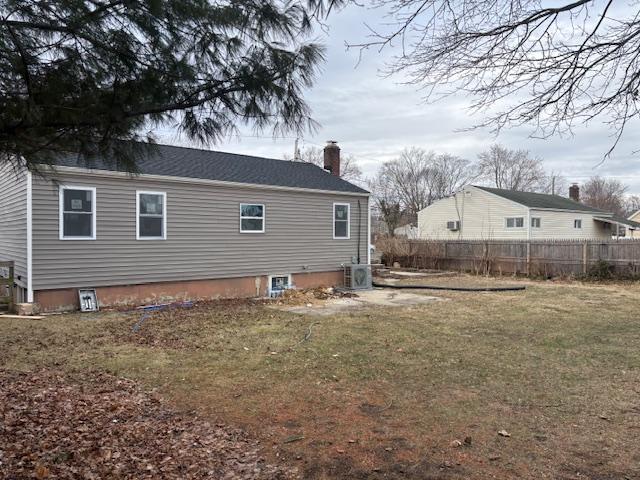 rear view of property featuring a chimney, fence, a lawn, and central air condition unit