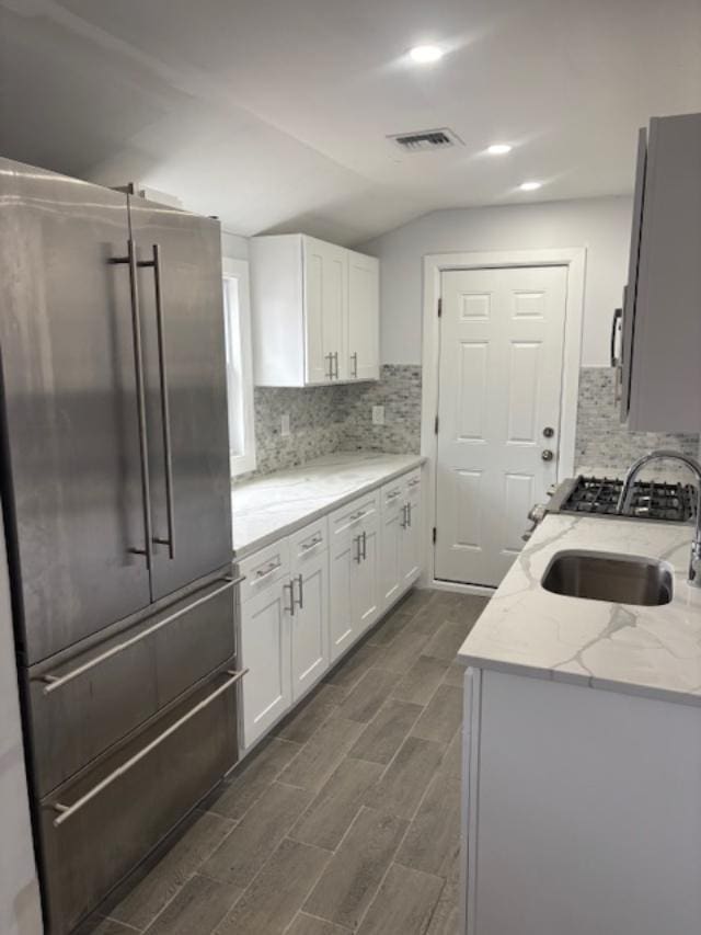 kitchen with a sink, white cabinetry, vaulted ceiling, and high end fridge