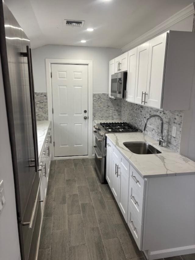 kitchen featuring visible vents, premium appliances, light stone countertops, white cabinetry, and a sink