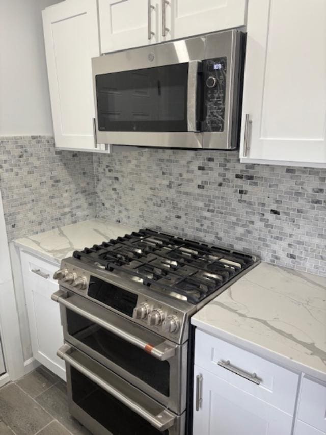 kitchen featuring appliances with stainless steel finishes, white cabinetry, backsplash, and light stone countertops