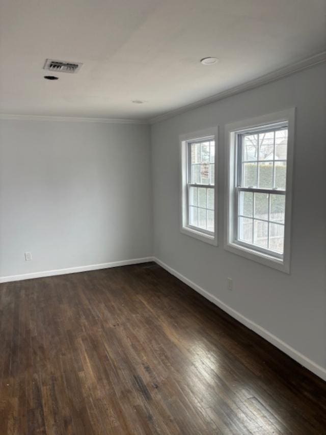 empty room featuring ornamental molding, visible vents, dark wood-type flooring, and baseboards