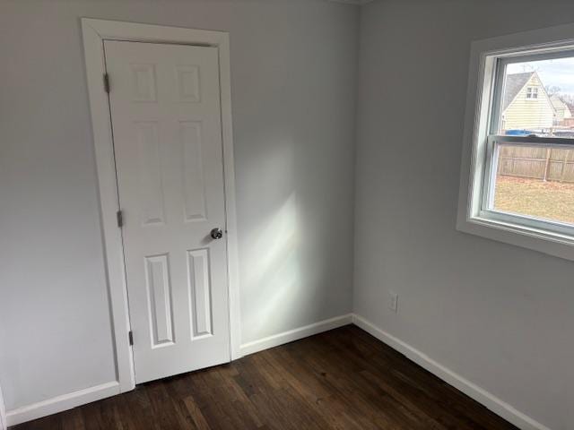 unfurnished bedroom with dark wood-style flooring, multiple windows, and baseboards