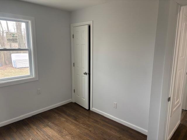 unfurnished bedroom featuring dark wood-style flooring, multiple windows, and baseboards