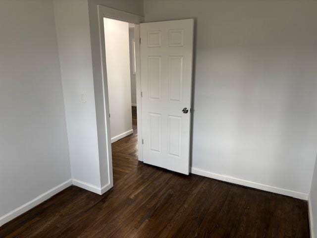 spare room featuring baseboards and dark wood-type flooring